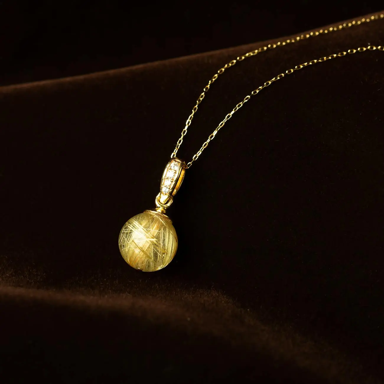Luxury gold pendant necklace with gemstone displayed on a dark velvet surface.