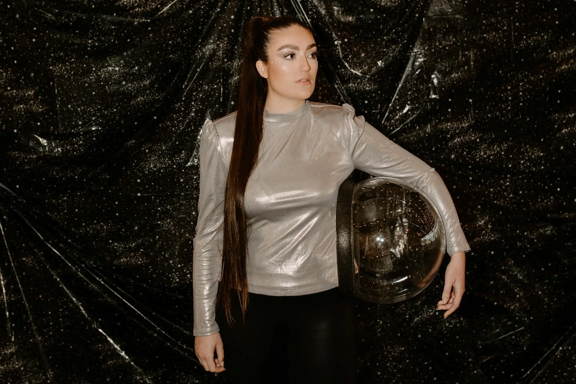 Elegant woman in a silver outfit with space-themed background holding a space helmet.