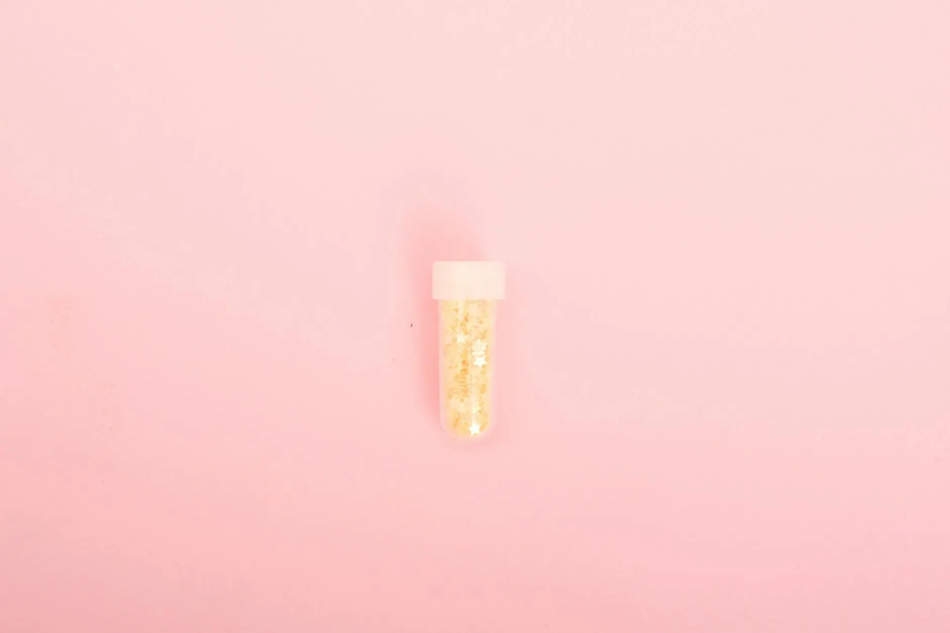 A small tube of golden glitter on a bright pink background, perfect for creative projects.